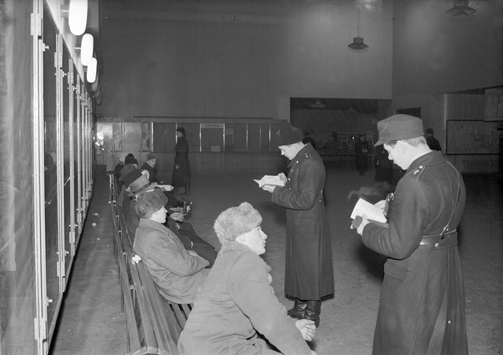 Armeijan "verikauha"-nimelläkin tunnettu kenttälakki tuli poliisin käyttöön vuodesta 1945. Väriltään lakki oli tummansininen, ja sen saumareunukset vastasivat asetakin kauluslaattojen väriä. Aluksi kenttälakkia käytettiin vain talvella. Matkustuslupien tarkastus Tampereen linja-autoasemalla. Kuvaaja: E.M. Staf, kuva: Museokeskus Vapriikki.