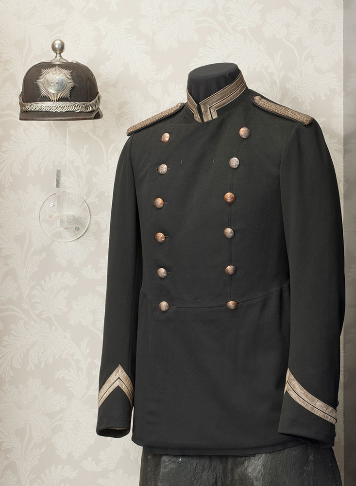 Kaupunkipoliisin virkapukuun m1906 kuului sortuutin lisäksi lyhyt asetakki, jota käyttivät ennen kaikkea poliisipäällystö ja ratsupoliisit. Puvulle tyypillinen päähine oli kaski-kypärä, jonka päällä oli metallinen nuppi. Ratsukomisarion asetakki esillä Poliisimuseon perusnäyttelyssä vuonna 2012. Kuva: Museokuva Matti Huuhka.