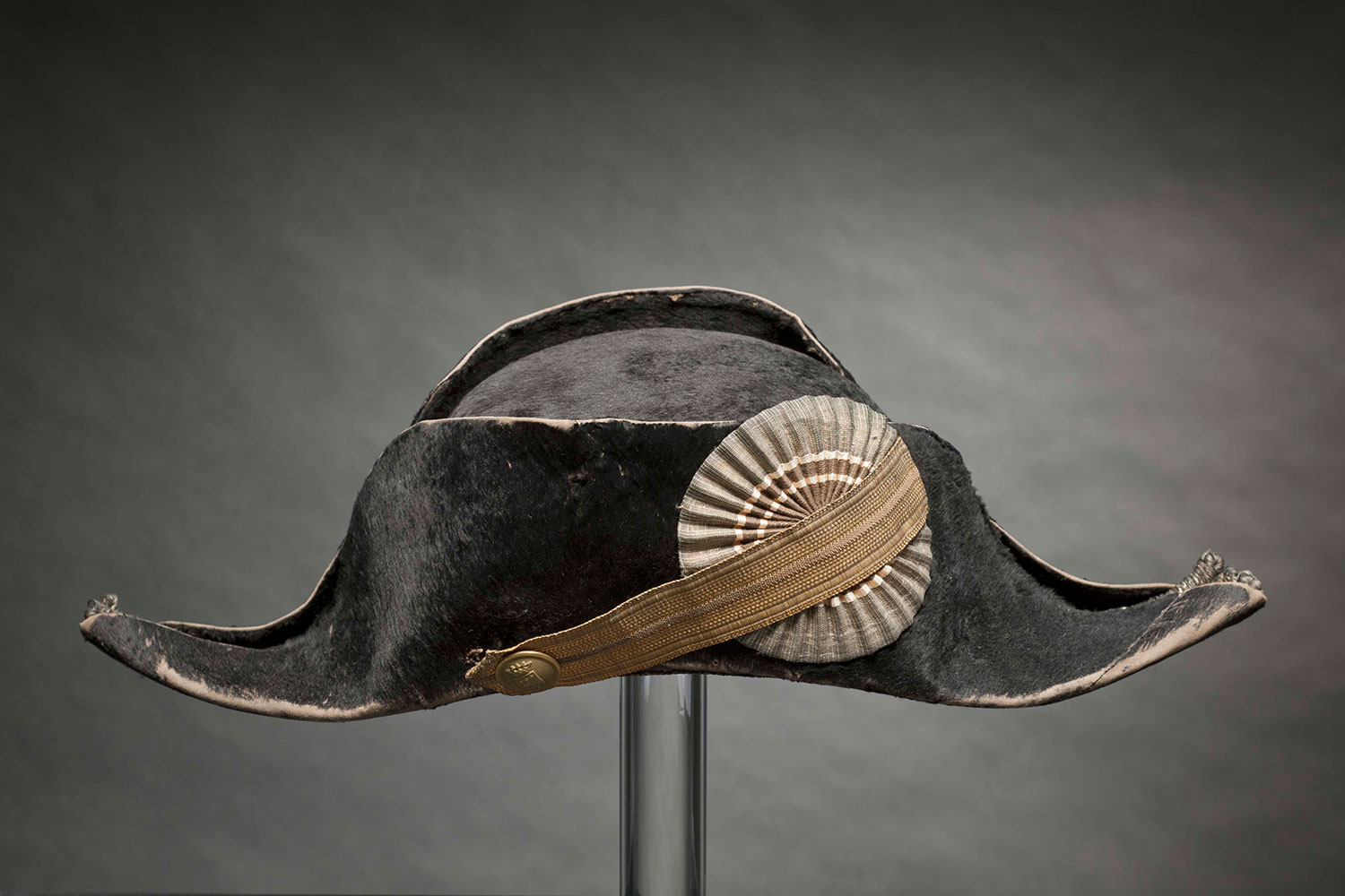 Läänien virkamiesten pukuun 1800-luvulla kuului hännystakin kanssa käytettävä kaksikolkkahattu. Samanlainen päähine kuului Helsingin poliisilaitoksen ylempien virkamiesten virkapukuun m1861. Vuosisadan loppua kohden hattu siirtyi enemmän juhlakäyttöön lipallisten virkalakkien yleistyessä arkikäytössä. Oriveden nimismies Carl Danielsin juhlalakki 1800-luvun lopulta. Kuva: Museokuva Matti Huuhka.