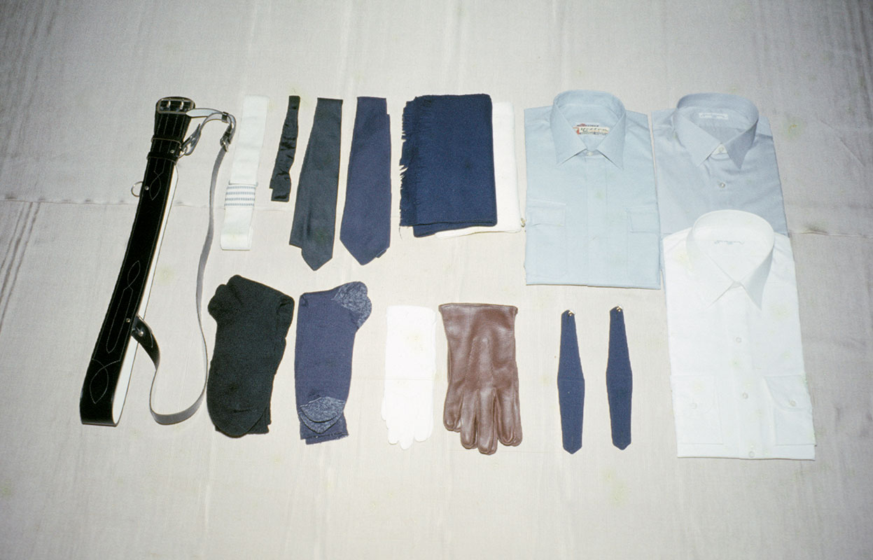 Poliisimiehen asusteet 1950-60-luvuilla. Kauluspaitoja oli kahta väriä ja niin oli myös solmioita: tummansinistä käytettiin harmaan ja mustaa valkoisen paidan kanssa. Juhlakäytössä myös musta solmuke oli mahdollinen.